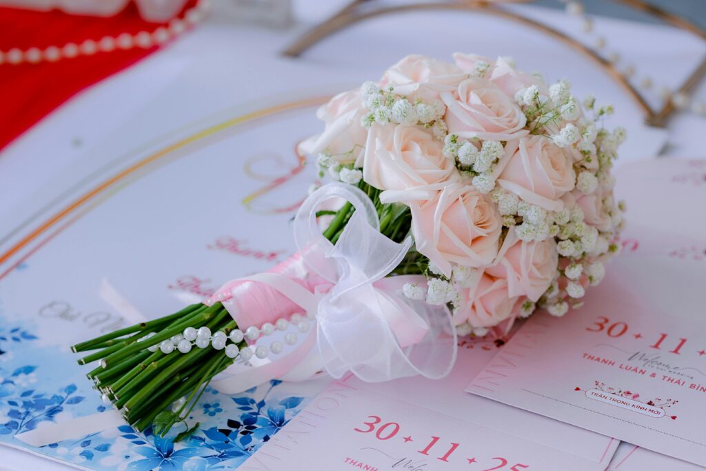Close-up of a pink rose bridal bouquet placed on elegant wedding invitations with pearls.